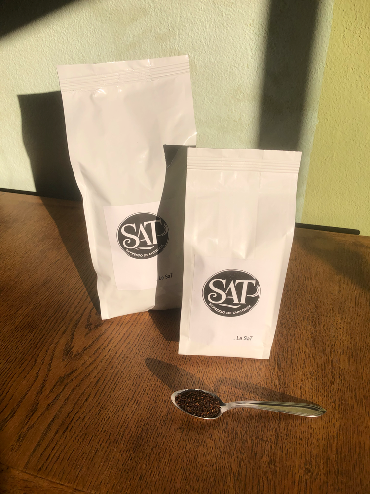 Deux sacs de SAT Expresso de chicorée sur table en bois, mur vert en arrière-plan, cuillère à café remplie de chicorée posée devant