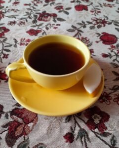 Tasse jaune de chicorée sur soucoupe avec calisson d'Aix, posée sur une nappe à motifs floraux